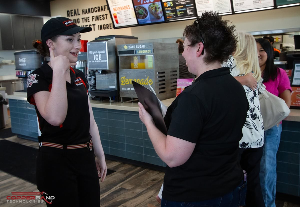 A McAlister's Deli team member talking with Liz Grant of Copperband during the July 2026 Quality Service Award presentation